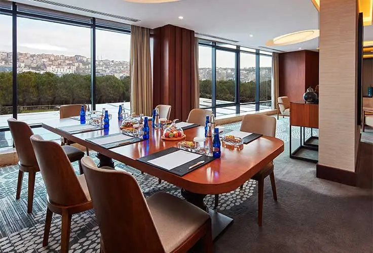 modern hotel meeting room setup with snacks, water bottles, and large windows overlooking city and greenery