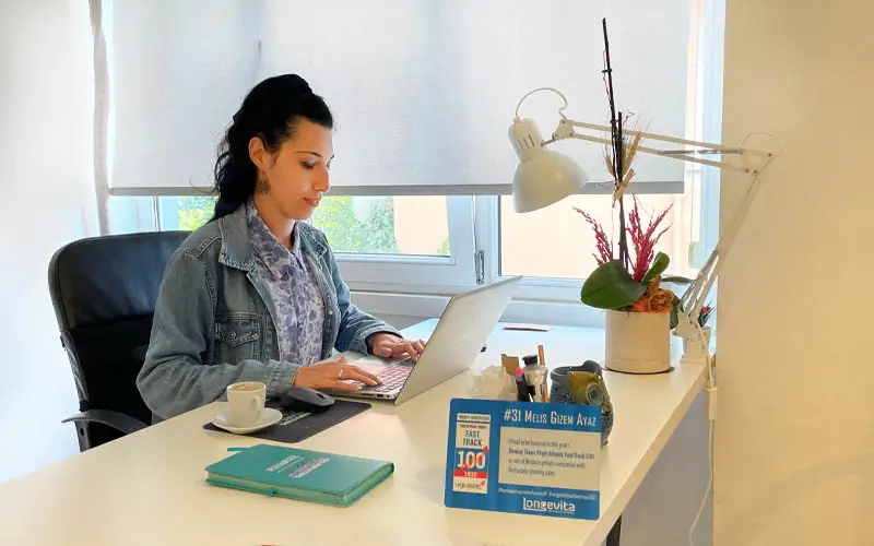 A woman working at a white desk on a computer.