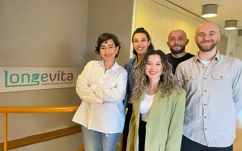 A group of co-workers standing next to a Longevita banner in an office.