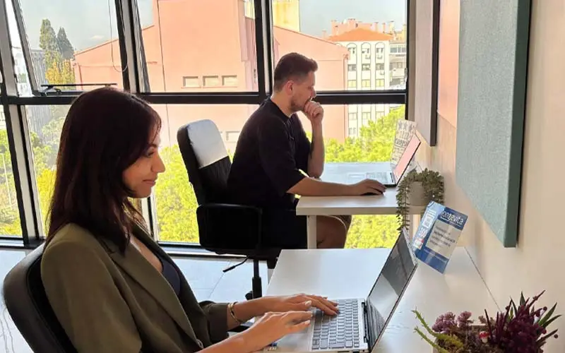 Two people working at their desks in an office area, focused on their computers.
