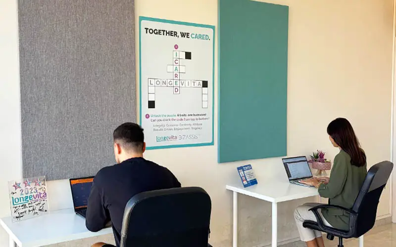 Two people working at their desks in an office area, focused on their computers.