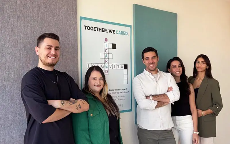 A group of co-workers standing next to a Longevita banner in an office.